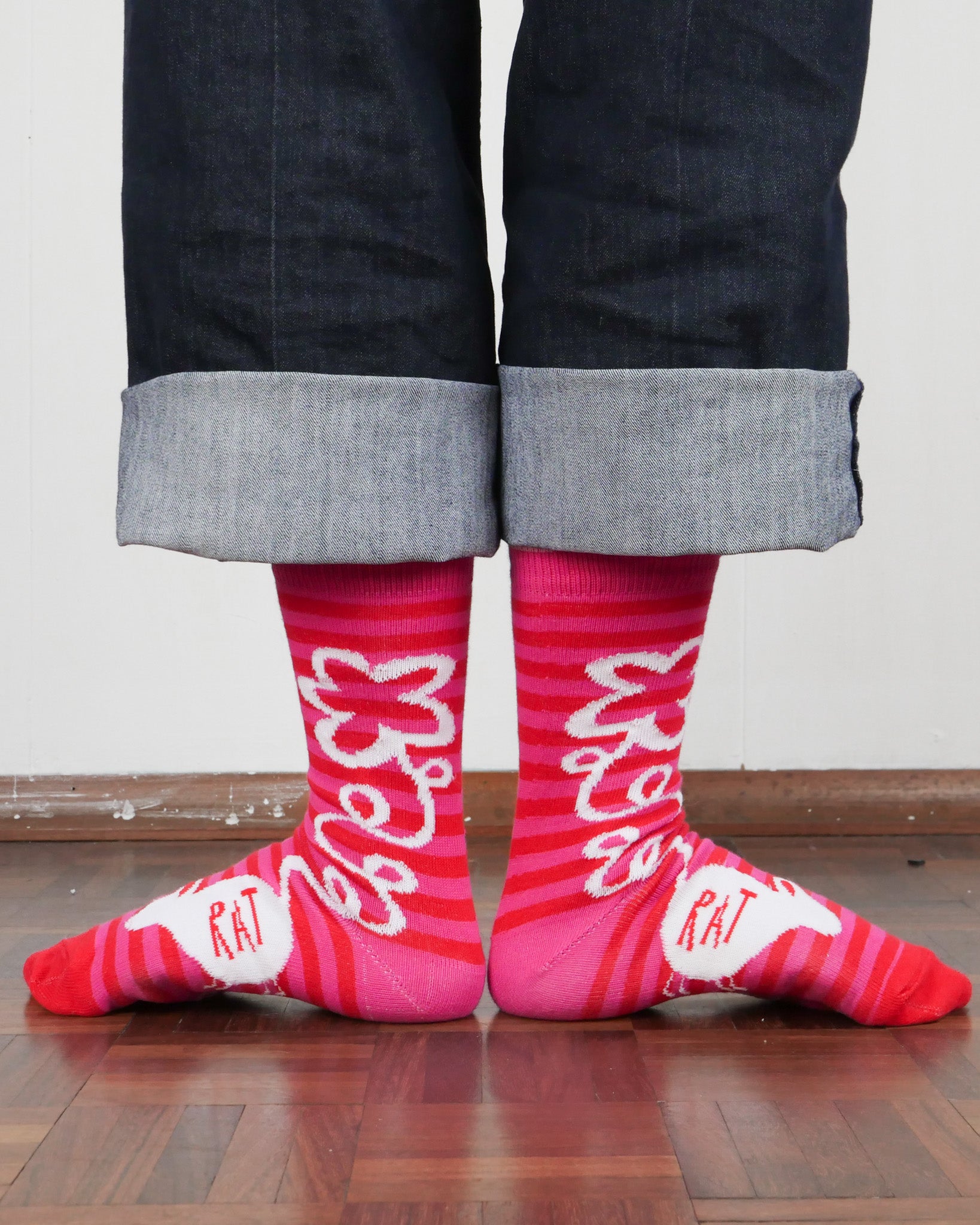 Person wearing red socks with white rat illustrations and text on a wooden floor.
